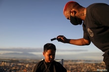 Barber Renan Estate gives a haircut to a child at home as part of his 