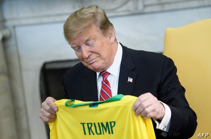 (FILES) In this file picture taken on March 19, 2019 US President Donald Trump looks at a soccer jersey given by Brazil's…