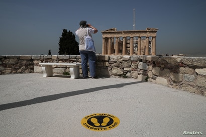 A visitor takes a photo of the Parthenon temple next to a social distancing marker, as the Acropolis archaeological site opens…