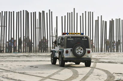 Un vehículo de la Patrulla Fronteriza permanece estacionado frente a un grupo de personas que mira desde el otro lado de la cerca limítrofe entre México y Estados Unidos en la zona conocida como Border Field State Park en San Diego.