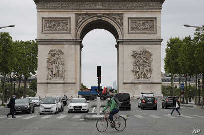 A person rides his bicycle in front of Arc de Triomphe, Monday, May 11, 2020 in Paris. he French began leaving their homes and…