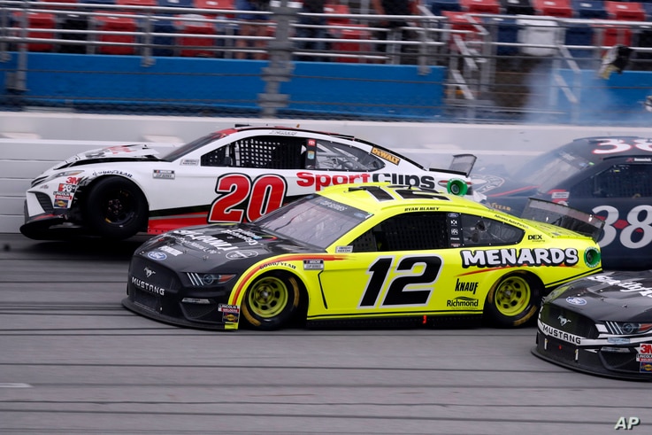 Winner Ryan Blaney (12) approaches the finish line as driver Erik Jones (20) crashes at the finish of a NASCAR Cup Series auto…