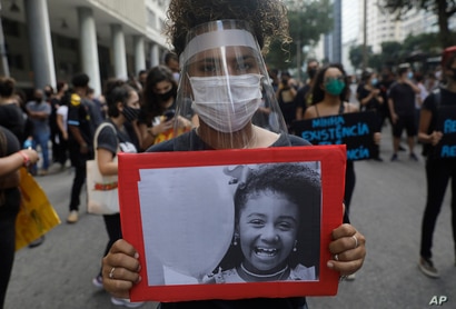 A woman wearing a face shield amid the new coronavirus pandemic holds a photo of Agatha, 8, a black child who was shot dead…
