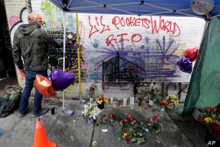 An artist at left works on a piece using spray paint and chalk, Tuesday, June 30, 2020, next to a growing memorial for a 16…